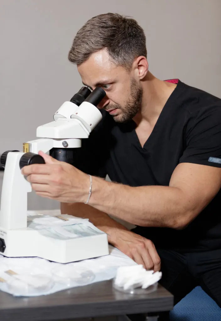 RESTORE technician examining follicular grafts under a microscope